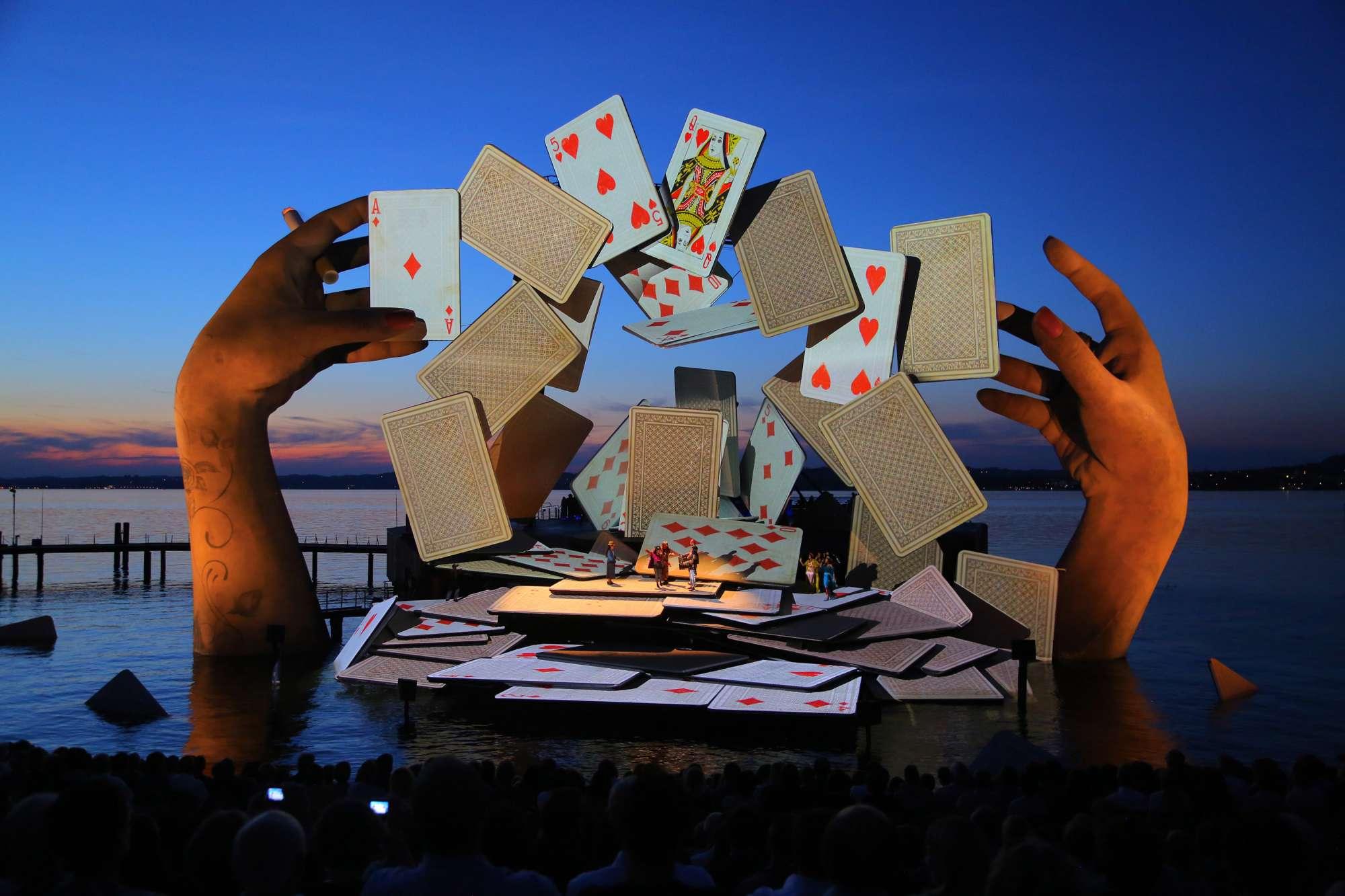 Scene from Es Devlin's Carmen set - playing card stage on river is flaked by large hands